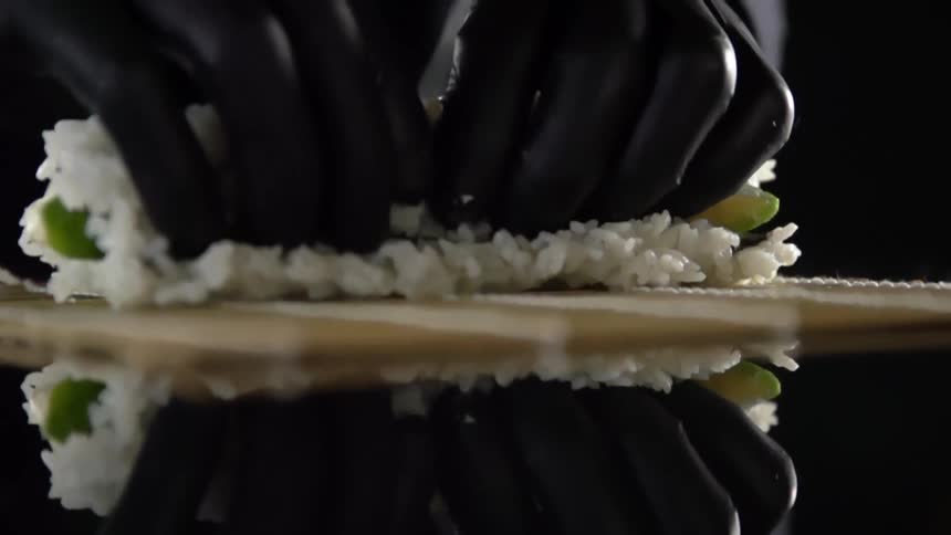Cook with black gloves rolls a sushi with boiled rice in studio