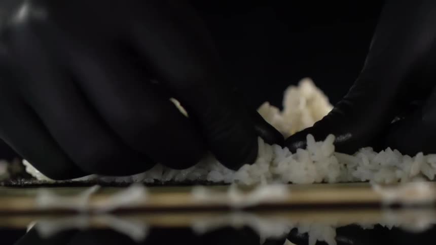 A person wearing black gloves presses down on rice with their thumbs