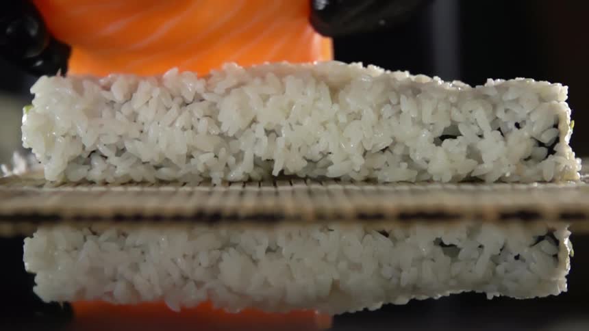 A person puts fish on a roll of rice as they make sushi