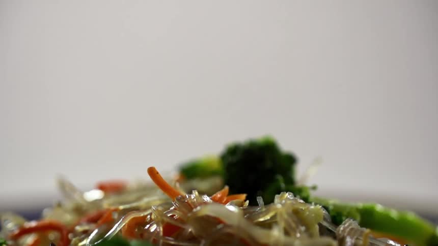 Green broccoli sprouts falling over glass noodles with sliced carrots