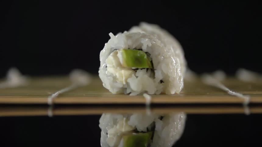 A chef tightens a roll of sushi filled with tuna and avocado on a bamboo mat