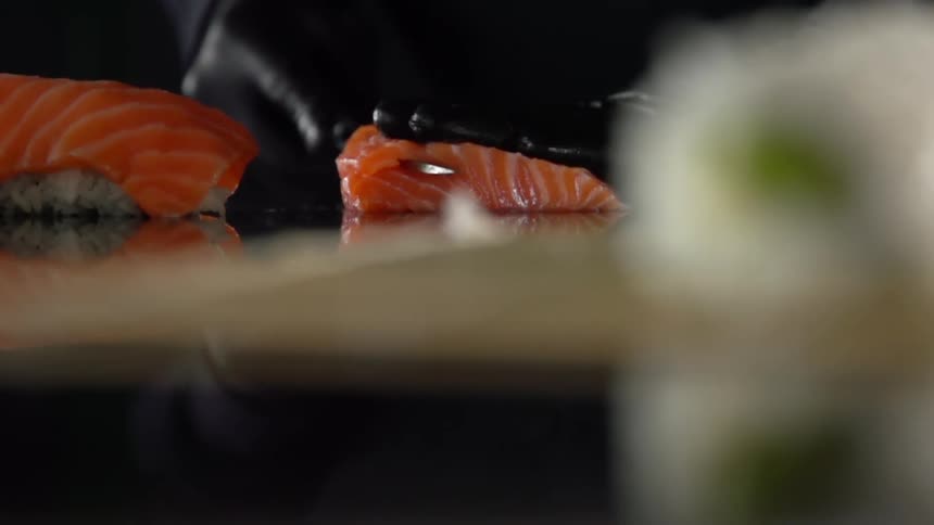 Cook with black gloves cuts fish for sushi