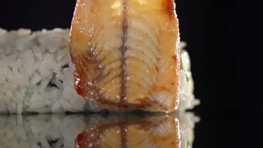 Glazed eel is added to the top of a sushi roll