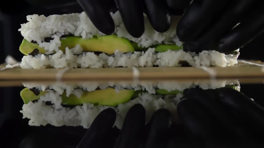 A person with black gloves prepares sushi