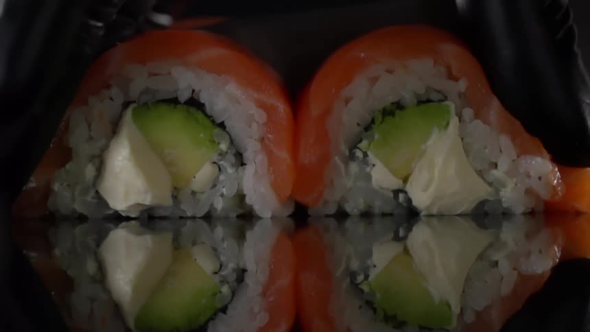 Cook with black gloves holds and cuts sushi in half in studio