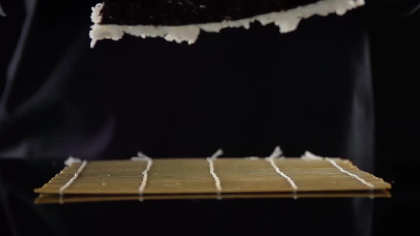 Black gloved hands lift a black paper with white fur attached and drops it onto a bamboo placemat