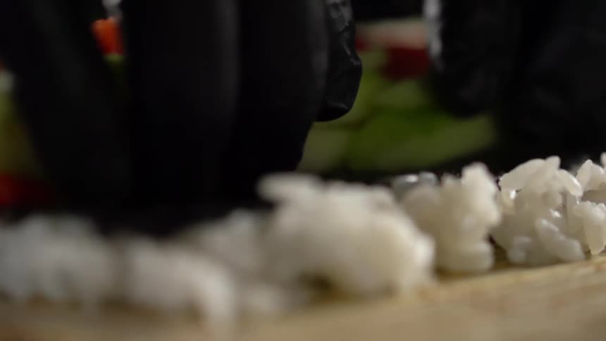 Close up of a man with black gloves making a sushi roll