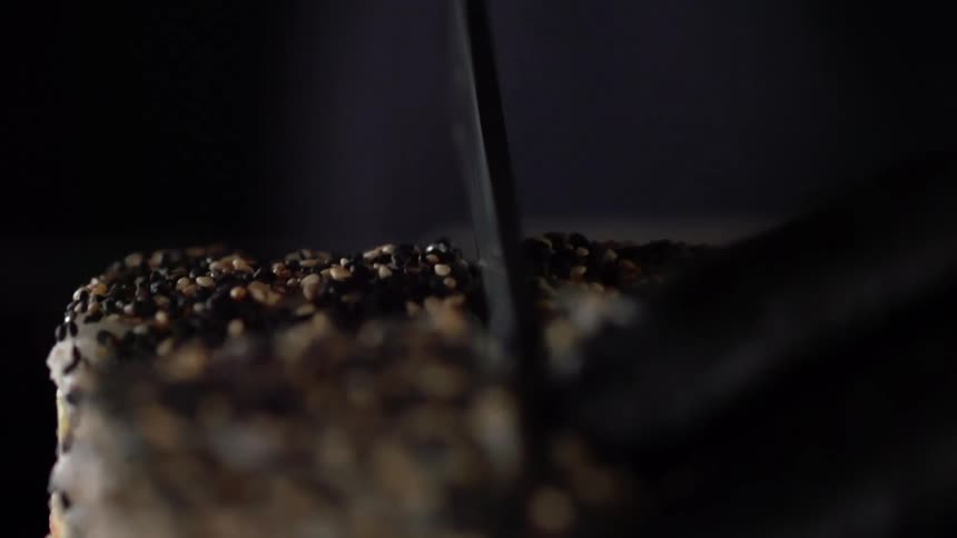 Food covered in seeds being cut with a knife by a person with gloves