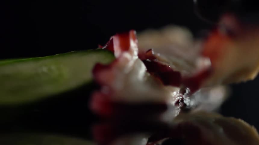 Black gloved hand sets food on top of another piece of food on a shiny surface