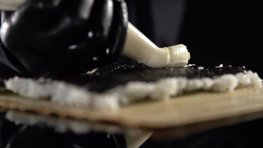 Chef wearing black latex gloves fills sushi with cream before rolling it with a bamboo mat