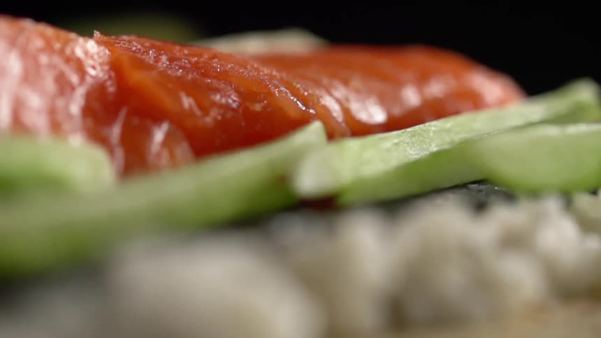 Sliced cucumber spears are dropped onto a surface in between sliced raw fish and cooked white rice