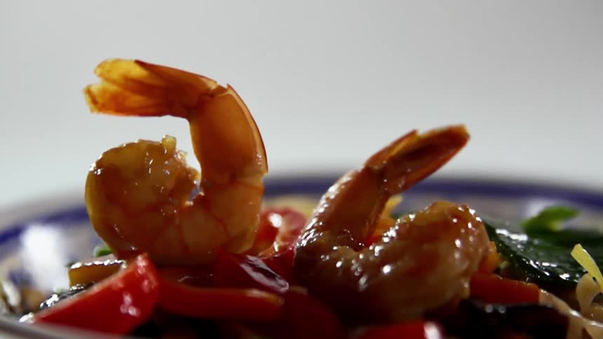 Cooked shrimp falls over vegetables in a ceramic bowl