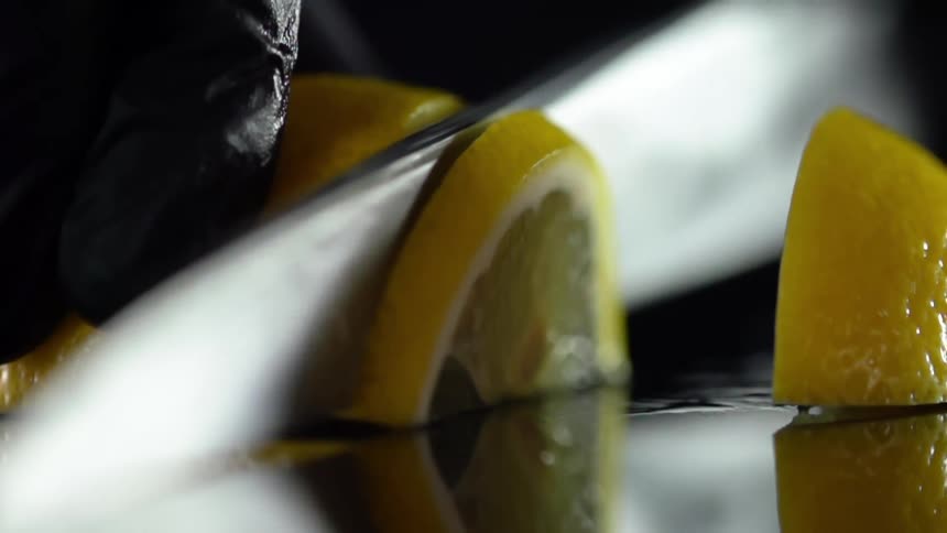 Cook with black gloves slices a lemon in studio