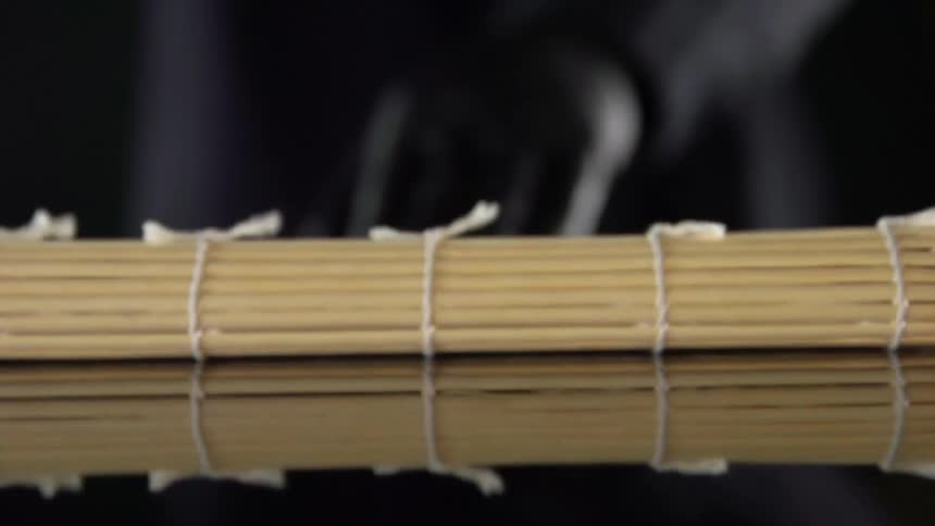 Cook with black gloves unrolls a bamboo mat to make sushi