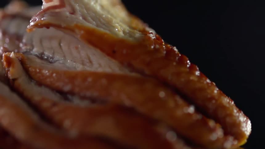 Fingers in a black glove move a piece of cooked poultry