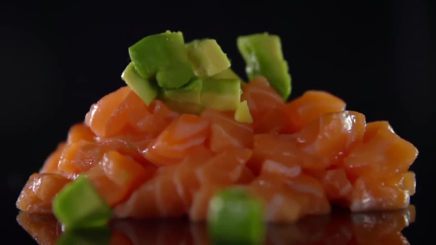 Finely chopped avocado bits fall over a pile of raw chopped salmon meat