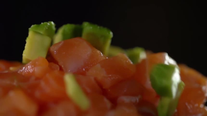 Diced vegetables falling atop a pile of diced raw fish