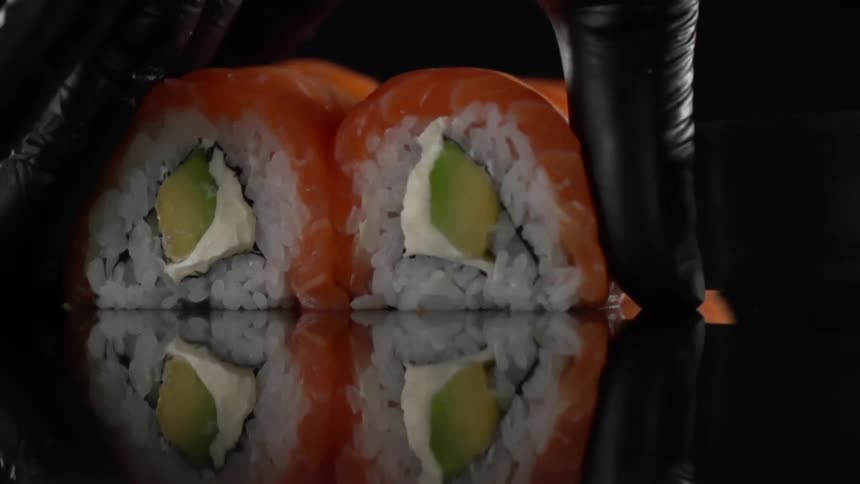 Man with black gloves cuts sushi rolls in half in studio