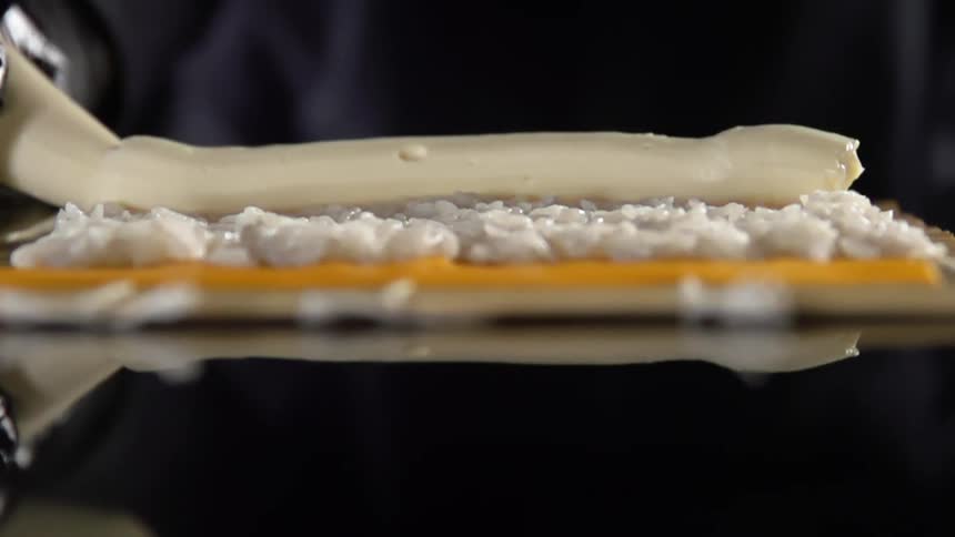 A think line of creamy sauce is piped onto sushi rice on a mat
