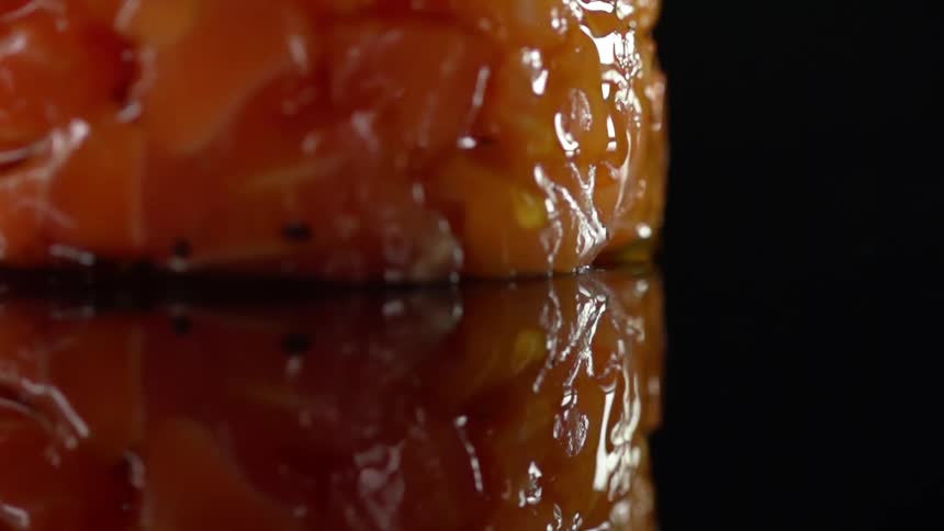 A drop of sauce rolls down the side of chopped salmon formed into a pattie sitting on a mirror surface