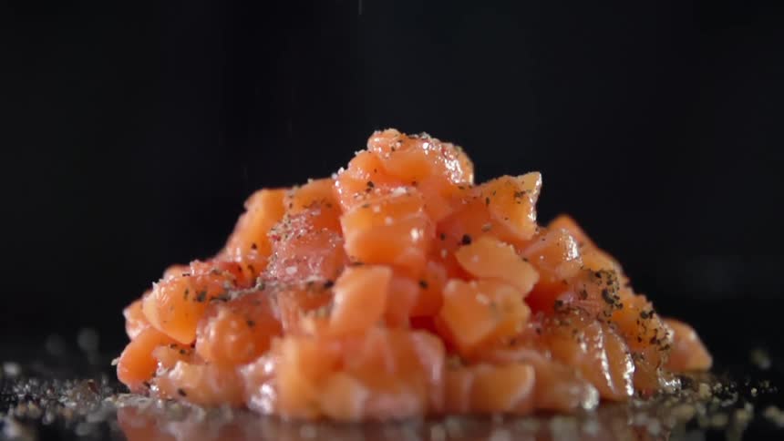 Seasoning drops onto piled food sitting on reflective surface