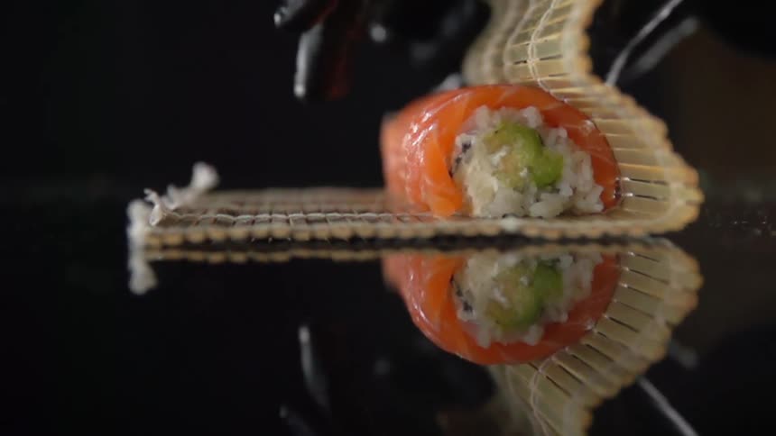A person wearing black plastic gloves peels a bamboo sushi rolling mat from around a rolled sushi and rice