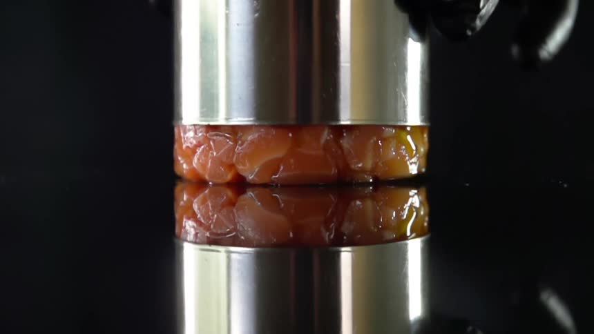 A metal cylinder being lifted to reveal the tightly packed diced fruit within