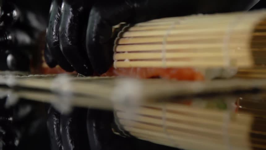 Person wears black gloves to form sushi with mat