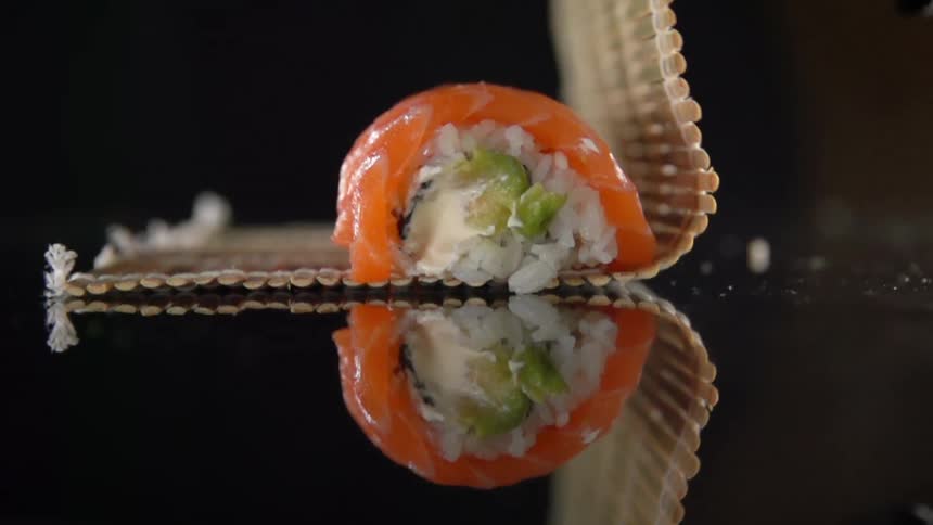 Gloved hands lift a bamboo sushi mat over a salmon roll