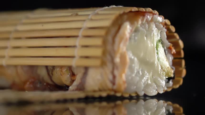 Sushi matdrops onto sushi roll sitting on reflecting flat black surface
