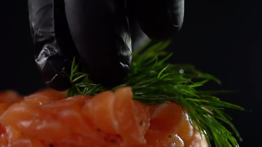 Close up of fresh dill being placed on raw pieces of chicken