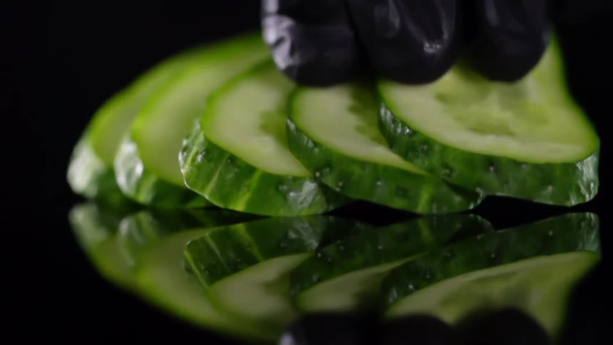 Sliced pickles being placed on reflective counter in slow motion