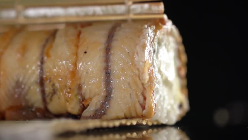 Sushi mat opens to show fish covered roll