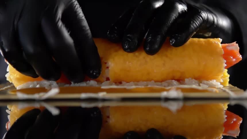 A person wearing black disposable gloves carefully prepares a sushi roll with their hands