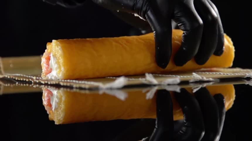 Man with black gloves places sushi on a bamboo mat to roll