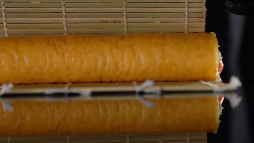 Chef wearing black latex gloves uses a bamboo mat to roll sushi