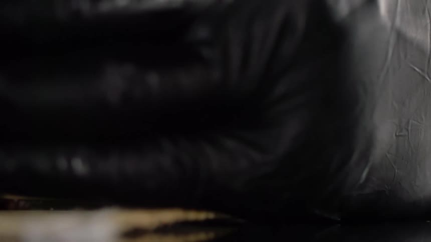 Gloved hands hold a sushi roll in a bamboo mat on a black mirror surface