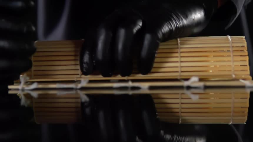 A person with black gloves wrapping sushi in bamboo