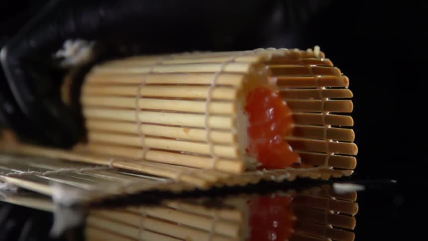 Cook with black gloves rolls sushi with bamboo mat