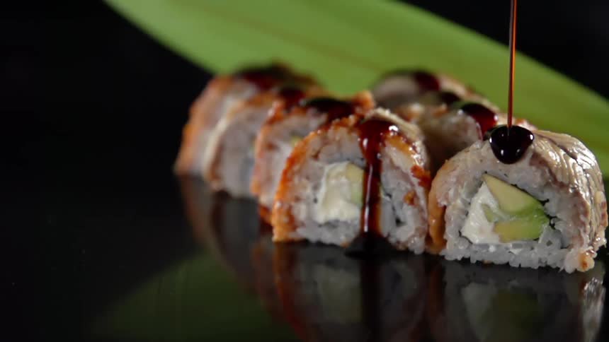 A dark brown sauce is drizzled over the top of several pieces of sushi