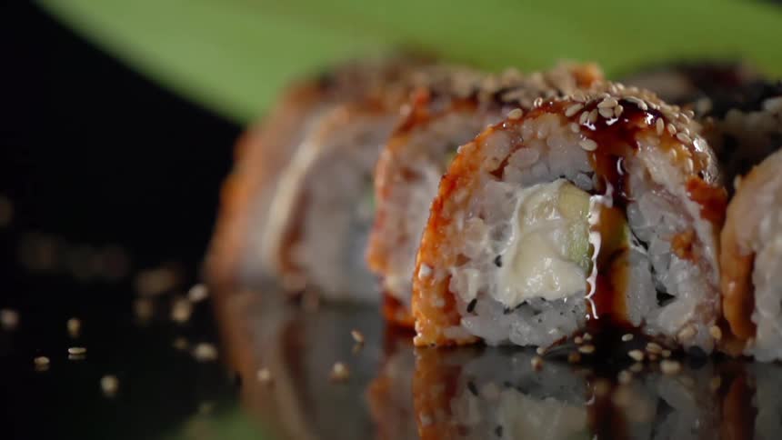Sesame seed falling over sushi rolls on a reflective surface
