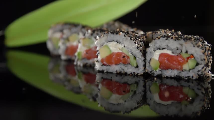 Sesame seeds falling over sushi rolls over a reflective surface