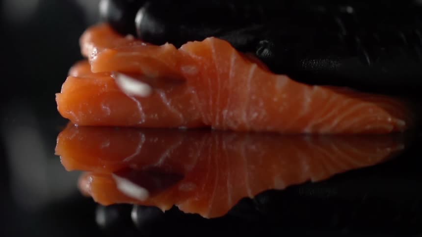 Man with black gloves cuts salmon with a sharp knife in studio