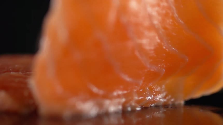 Slices of salmon meat being turned over on a reflective surface