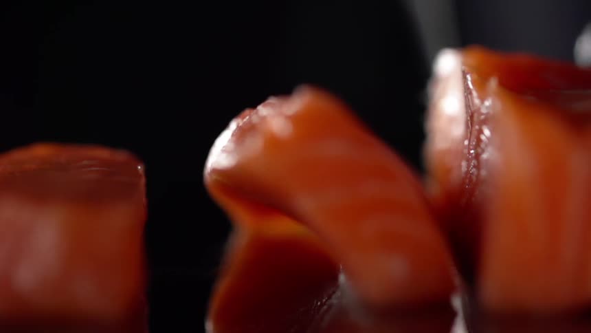 Man wearing black gloves cuts fish for sushi in studio