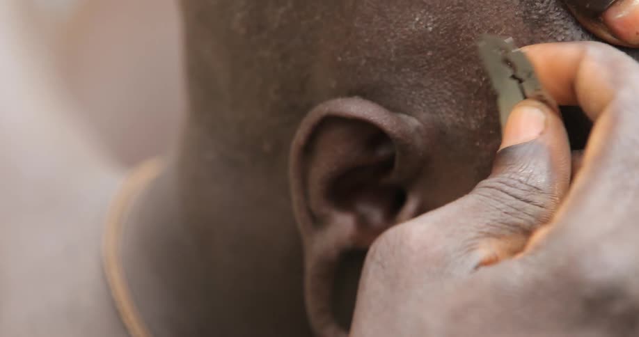 A man using a razor blade to shave another man's head