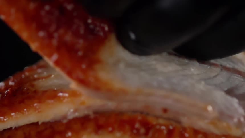 Slices of cooked fish are piled up by a hand in a black latex glove