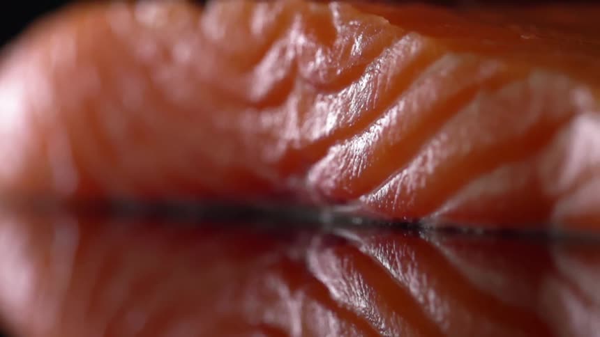 Extreme close up of a slice of salmon meat over a reflective surface