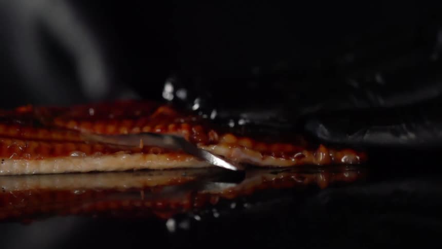 Chef wearing latex gloves slices meat with a kitchen knife over a reflecting surface