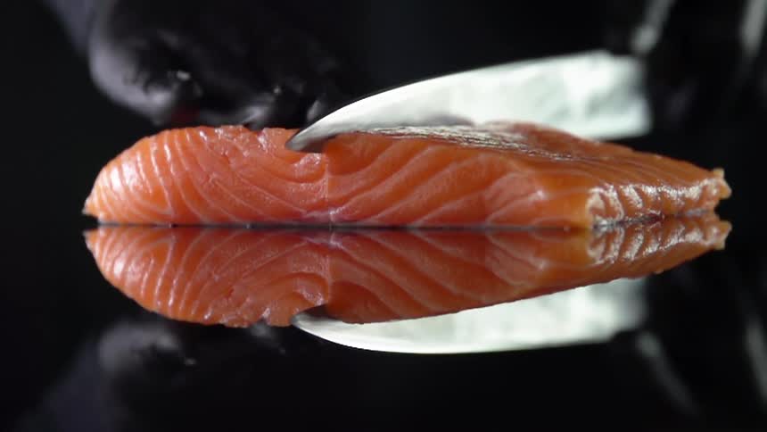 Cook with black gloves cuts salmon for sushi